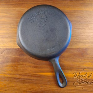 May include: A black cast iron skillet with a handle, stamped with "Wagner Ware Sidney -O-" and "1053G". The skillet is on a wooden surface. The handle has a hole for hanging.