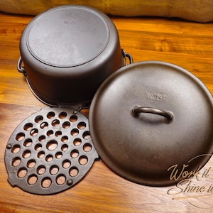 May include: A cast iron Dutch oven set with a lid, pot, and trivet. The set is dark brown and sits on a wooden surface. The lid has a handle and the trivet has multiple holes. The text "N 8" is visible on the lid and pot.