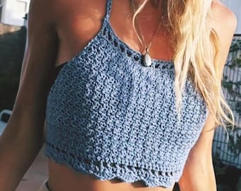 Puede incluir: Top halter de ganchillo azul claro con borde festoneado. El top está hecho a mano con un punto texturizado y presenta un diseño de cuello halter. También es visible un collar plateado con un colgante.