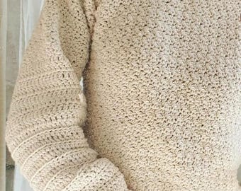 May include: A beige crochet sweater with long sleeves. The sleeves have a ribbed cuff design. The sweater is made of a textured yarn and has a crew neck. The overall style is casual and handmade.