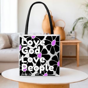 May include: A white tote bag with black handles featuring a floral pattern of black flowers with pink centers. The words "Love God Love People" are printed in white, with "John 13:34-35" below.