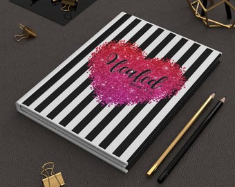 May include: A black and white striped notebook with a pink glitter heart that says "Healed" in white text. The notebook is on a gray surface with two pencils and gold paper clips.