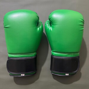 May include: Pair of bright green boxing gloves with black wrist straps. The gloves are made of a smooth material and are designed for protection during training or competition. The gloves are shown against a neutral background.