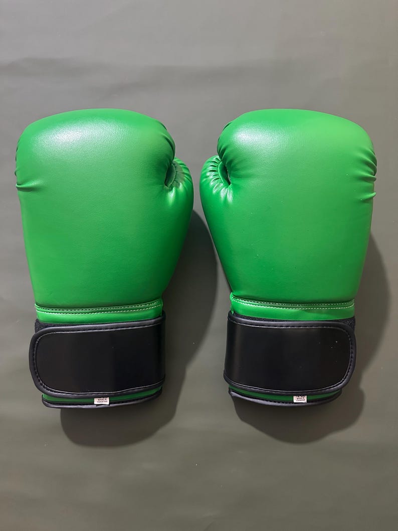 May include: Pair of bright green boxing gloves with black wrist straps. The gloves are made of a smooth material and are designed for protection during training or competition. The gloves are shown against a neutral background.