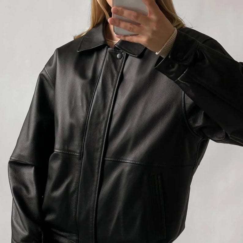 Pode incluir: Casaco de couro preto com gola e fecho de bot&atilde;o. O casaco tem um estilo bomber cl&aacute;ssico com um bolso frontal e um ajuste descontra&iacute;do. As mangas s&atilde;o compridas e o couro parece liso.