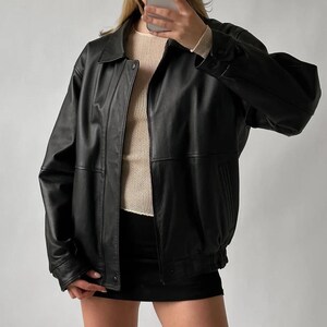 Pode incluir: Casaco de couro preto com gola, fechos de bot&atilde;o e fecho de correr. O casaco tem um corte estilo bomber com punhos e bainha el&aacute;sticos. Por baixo, &eacute; usado um su&eacute;ter creme.