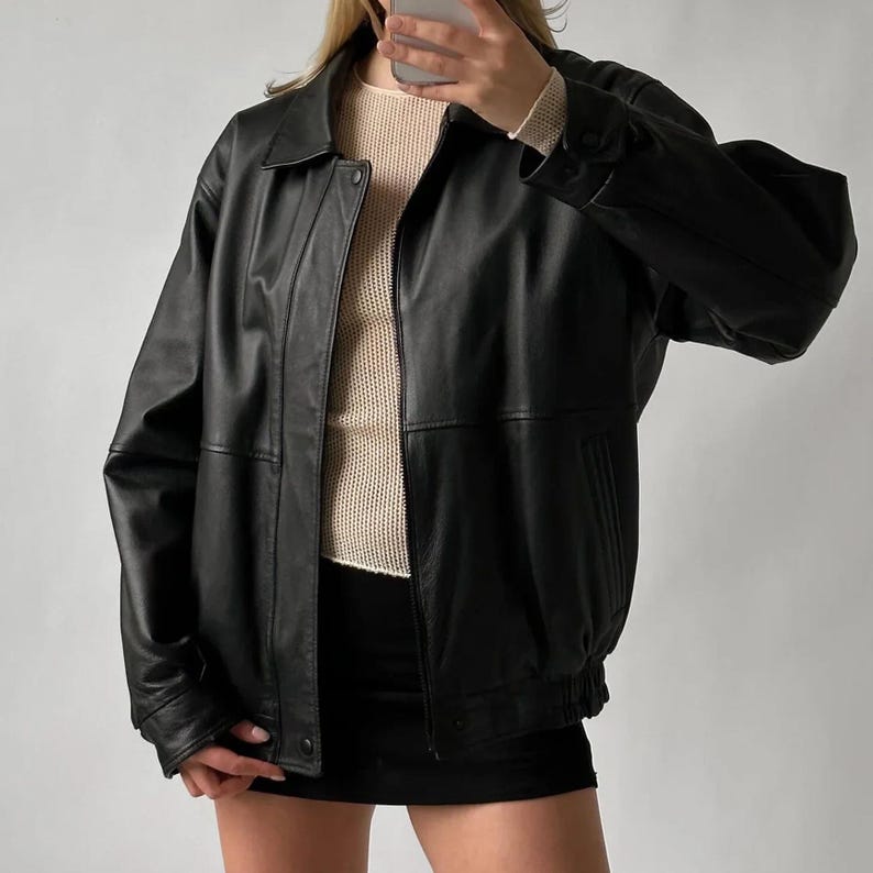 Pode incluir: Casaco de couro preto com gola, fechos de bot&atilde;o e fecho de correr. O casaco tem um corte estilo bomber com punhos e bainha el&aacute;sticos. Por baixo, &eacute; usado um su&eacute;ter creme.