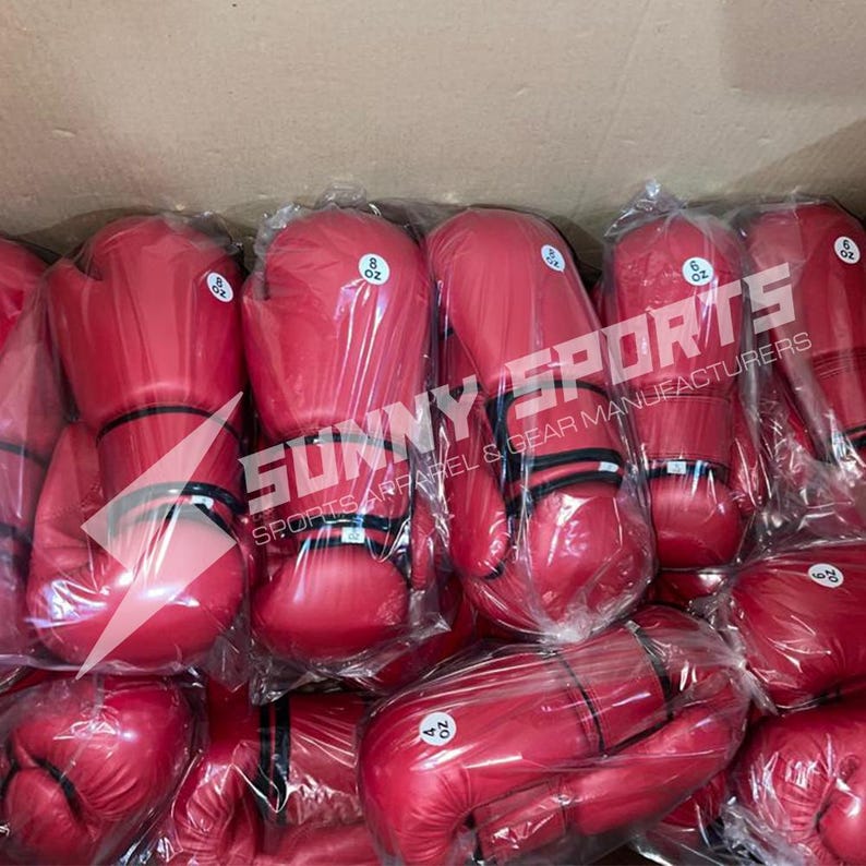 May include: A collection of red boxing gloves, some labeled 8 oz and 4 oz, are packaged in clear plastic. The gloves are stacked inside a cardboard box. The text "SUNNY SPORTS SPORTS APPAREL & GEAR MANUFACTURERS" is visible.