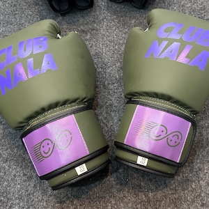 May include: Olive green boxing gloves with the text "CLUB NALA" in purple. The wrist straps are purple with a smiley face design and the text "10 OZ".