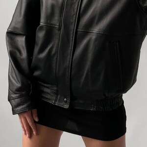 Pode incluir: Casaco de couro preto estilo bomber. O casaco apresenta bainha e punhos canelados, fecho de bot&atilde;o e gola cl&aacute;ssica. A pe&ccedil;a &eacute; usada com uma minissaia preta.