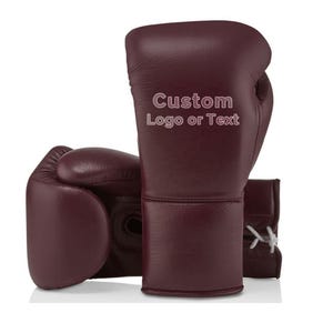 May include: Burgundy leather boxing gloves with the text "Custom Logo or Text" printed on the side. The gloves are shown on a white background. The gloves have white laces and are designed for boxing.