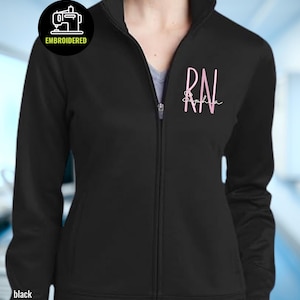 May include: Black zip-up jacket with pink "RN" script and "Sophia" below. A circular logo with a sewing machine and "EMBROIDERED" is on the upper left. The word "black" is at the bottom left.