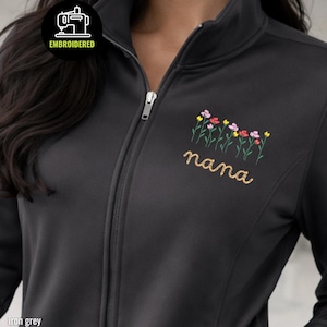 May include: Iron grey zip-up jacket with embroidered floral design and the word "nana" in gold thread. The jacket features a high collar and a full-length zipper. The embroidered flowers are in shades of pink, yellow, and red.