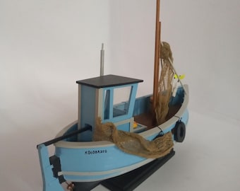 Puede incluir: Un modelo de barco de pesca de madera azul y blanco con una red marrón y un neumático negro. El barco está sobre una base de madera negra y tiene la palabra "Kolobrzeg" escrita en el lateral.