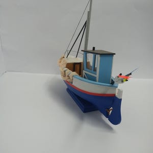 Könnte beinhalten: Miniatur-Holzboot in Blau, Weiß und Rot bemalt. Das Modellboot hat eine kleine Kabine, einen Mast und Seildetails. Es ist ein dekoratives Objekt.