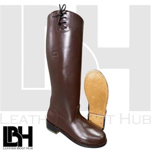 Könnte beinhalten: Ein Paar braune Lederreitstiefel. Ein Stiefel steht aufrecht und zeigt die volle Länge und die Schnürdetails oben. Der andere Stiefel liegt auf der Seite und zeigt die Sohle. Die Stiefel sind in einem satten, dunklen Braun gehalten.