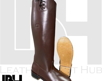 Puede incluir: Un par de botas de montar de cuero marrón. Una bota está de pie, mostrando toda la longitud y los detalles de los cordones en la parte superior. La otra bota está tumbada de lado, revelando la suela. Las botas son de un rico color marrón oscuro.