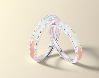 May include: Two silver rings with a colorful design. The rings have a wave-like pattern with pastel colors, including light blue, yellow, and orange. The rings are set against a soft, neutral background.