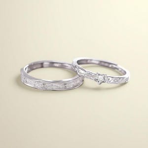 Pode incluir: Dois anéis de prata. Um anel apresenta uma banda texturizada com um design ondulado. O outro anel tem um design em forma de estrela com uma pequena pedra preciosa no centro e pequenas pedras preciosas adicionais ao longo da banda. Ambos os anéis estão em um fundo bege claro.