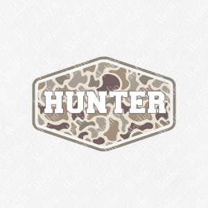 May include: A badge-shaped design with the word "HUNTER" in bold, white letters. The background features a camouflage pattern in shades of brown, tan, and gray. The badge is outlined in a darker brown color.