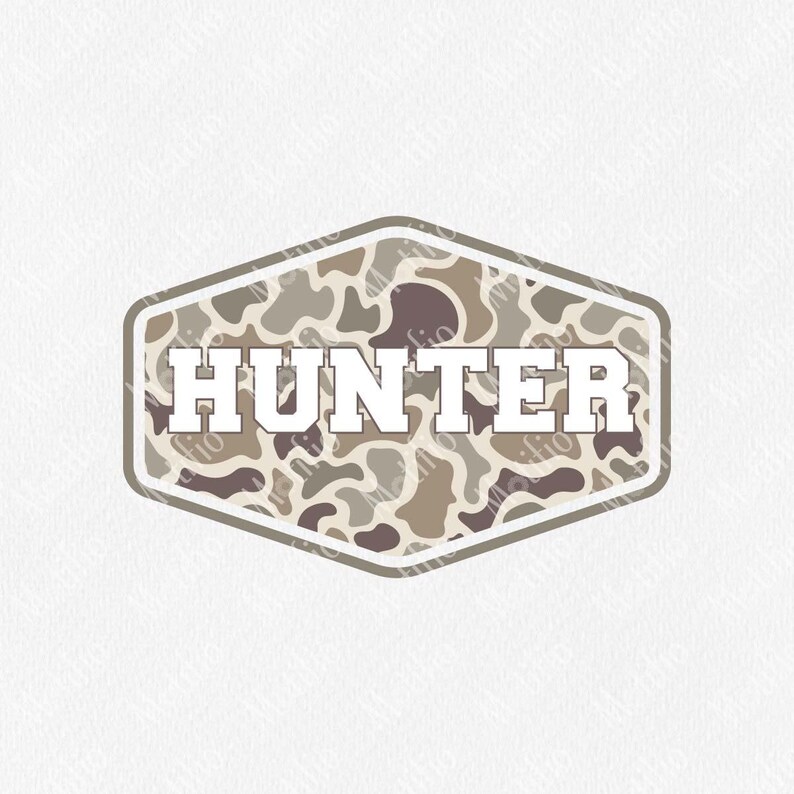 May include: A badge-shaped design with the word "HUNTER" in bold, white letters. The background features a camouflage pattern in shades of brown, tan, and gray. The badge is outlined in a darker brown color.