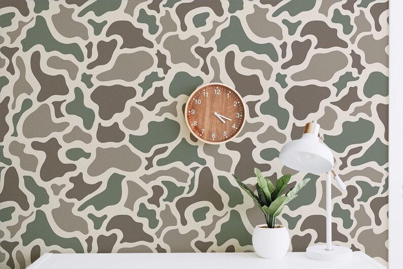 May include: A room with a camouflage pattern wallpaper in shades of green, brown, and gray. A round wooden clock hangs on the wall, and a white desk lamp and potted plant sit on a white surface.
