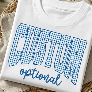 Op de afbeelding: Een wit t-shirt met ronde hals voorzien van het woord CUSTOM in grote, blokvormige, blauw-wit geblokte letters met een donkerblauwe omlijning. Daaronder staat het woord optional in een kleiner, blauw, cursief lettertype.