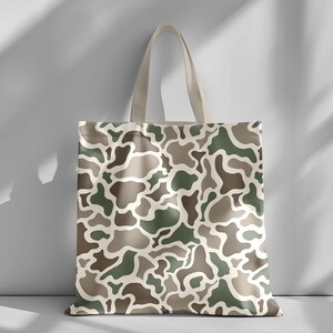 May include: A canvas tote bag featuring a camouflage pattern in shades of green, brown, and beige. The bag has a rectangular shape with a matching beige handle. The camouflage design covers the entire surface of the bag.