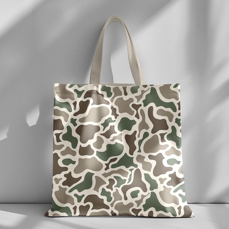 May include: A canvas tote bag featuring a camouflage pattern in shades of green, brown, and beige. The bag has a rectangular shape with a matching beige handle. The camouflage design covers the entire surface of the bag.