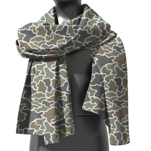 May include: A camouflage pattern scarf in shades of green, brown, gray, and white. The scarf is draped over a mannequin, showcasing its design and texture. The fabric appears soft and lightweight, suitable for various weather conditions.