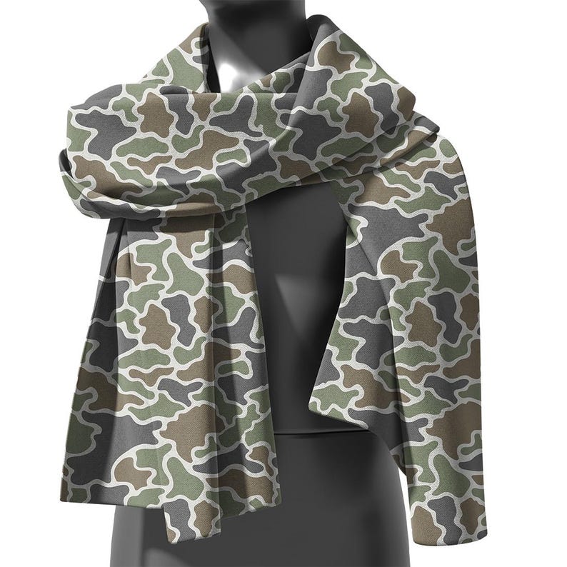 May include: A camouflage pattern scarf in shades of green, brown, gray, and white. The scarf is draped over a mannequin, showcasing its design and texture. The fabric appears soft and lightweight, suitable for various weather conditions.