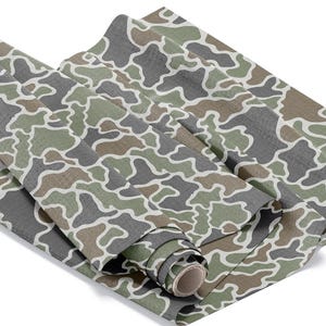 May include: Rolled fabric with a camouflage pattern in shades of green, gray, and brown, outlined in white. The fabric is partially rolled, revealing the cardboard core. The pattern is a classic military-inspired design.