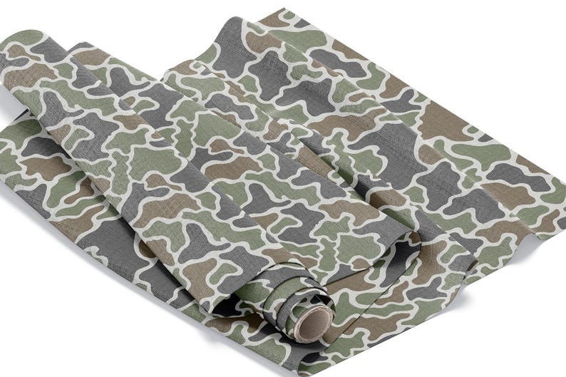 May include: Rolled fabric with a camouflage pattern in shades of green, gray, and brown, outlined in white. The fabric is partially rolled, revealing the cardboard core. The pattern is a classic military-inspired design.