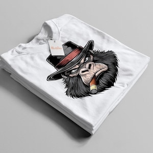 Könnte beinhalten: Weißes T-Shirt mit einer Illustration eines Gorillas, der einen schwarzen Hut mit rotem Band trägt und eine Zigarre raucht. Das T-Shirt ist gefaltet und gestapelt, mit einem Etikett "Motifin".