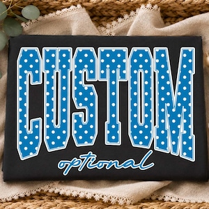 May include: A black t-shirt featuring the word CUSTOM in large, blue, block-style letters with a white polka dot pattern and a white outline. Below the word CUSTOM, the word optional is printed in a blue, cursive, script-style font.