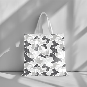 May include: A white tote bag with a repeating camouflage pattern in shades of gray. The bag has a simple design with a rectangular body and two white handles. The camouflage pattern has a distressed, textured look.