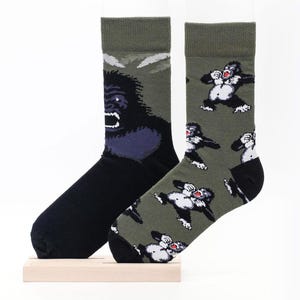 May include: A pair of socks with a gorilla print. One sock features a large gorilla face, while the other sock has a repeating pattern of smaller gorillas. The socks are green and black.