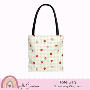 Könnte beinhalten: Eine Tragetasche mit hellgrünem Vichy-Muster und roten Erdbeeren. Die Tasche hat schwarze Griffe und den Text "Tote Bag Strawberry Gingham" unten. Ein helles, fröhliches Design.
