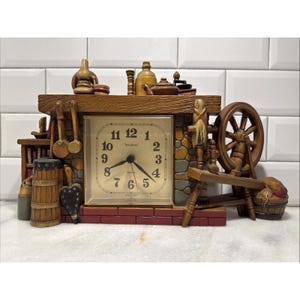 May include: A decorative clock with a rustic design. The clock face is square with black numerals and hands. The clock is surrounded by a wooden frame with miniature kitchen tools, a spinning wheel, and a small bookshelf. The clock reads "New Haven".