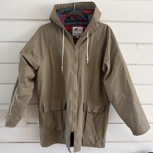 May include: A tan hooded jacket with a full-length zipper and two front pockets. The jacket has a plaid lining in the hood and a white drawstring. The brand name "Misty Harbor" is visible on the chest.