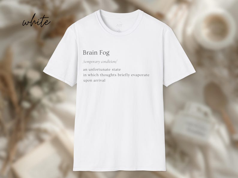 Puede incluir: Camiseta blanca con el texto "Brain Fog" y su definici&oacute;n. La definici&oacute;n describe un estado temporal en el que los pensamientos se evaporan brevemente. La palabra "white" est&aacute; escrita en cursiva en la esquina superior izquierda.