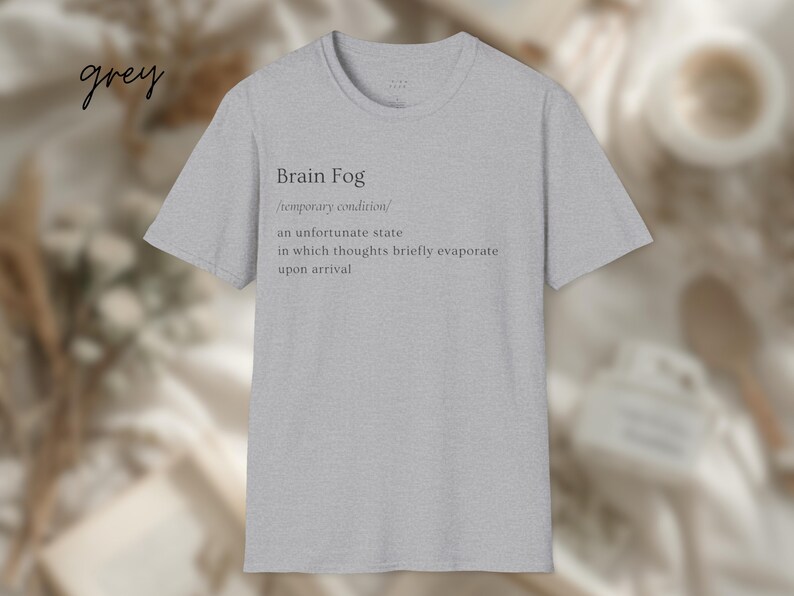 Puede incluir: Camiseta gris claro con la frase "Brain Fog" y su definici&oacute;n en texto negro. La definici&oacute;n describe una condici&oacute;n temporal donde los pensamientos se evaporan brevemente. La palabra "grey" est&aacute; escrita en cursiva en la esquina superior izquierda.