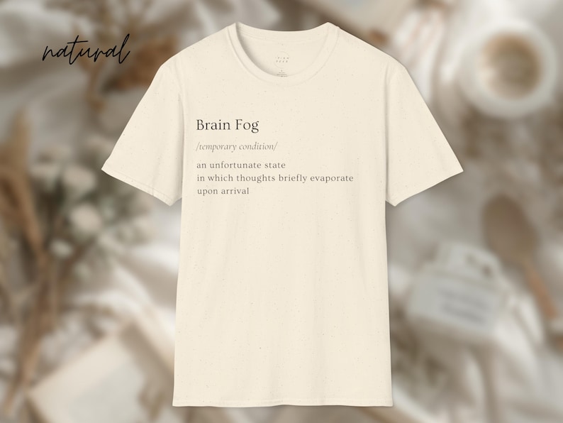 Puede incluir: Camiseta color crema con el texto "Brain Fog" y una definici&oacute;n. La definici&oacute;n describe una condici&oacute;n temporal donde los pensamientos se evaporan brevemente. La palabra "natural" est&aacute; escrita en cursiva.
