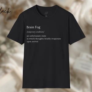 Puede incluir: Camiseta negra con el texto "Brain Fog" y una definici&oacute;n. La definici&oacute;n describe la niebla mental como una condici&oacute;n temporal donde los pensamientos se evaporan brevemente. La palabra "black" est&aacute; escrita en cursiva arriba a la izquierda.