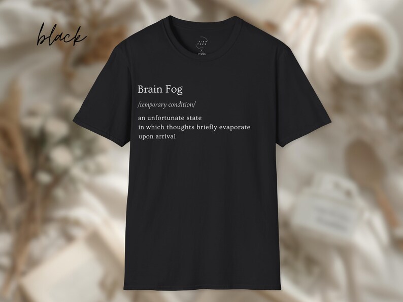 Puede incluir: Camiseta negra con el texto "Brain Fog" y una definici&oacute;n. La definici&oacute;n describe la niebla mental como una condici&oacute;n temporal donde los pensamientos se evaporan brevemente. La palabra "black" est&aacute; escrita en cursiva arriba a la izquierda.