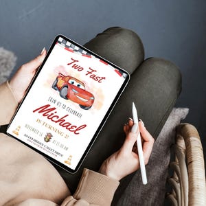K&ouml;nnte beinhalten: Ein Tablet-Bildschirm zeigt eine Geburtstagseinladung mit einer roten Rennwagen-Illustration. Der Text lautet "Two Fast" und "Feiern Sie mit uns Michael wird 2!" mit Datum und Uhrzeit.