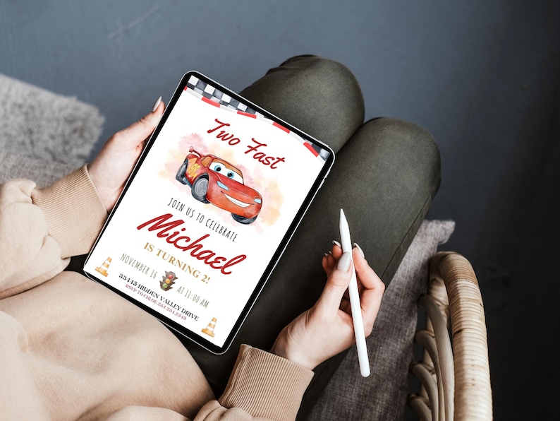 K&ouml;nnte beinhalten: Ein Tablet-Bildschirm zeigt eine Geburtstagseinladung mit einer roten Rennwagen-Illustration. Der Text lautet "Two Fast" und "Feiern Sie mit uns Michael wird 2!" mit Datum und Uhrzeit.