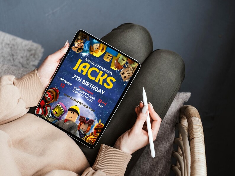 May include: A tablet displaying a birthday invitation with the text "JACKS 7TH BIRTHDAY". The invitation features cartoon characters and the date "OCTOBER 12". A stylus is held in the hand.