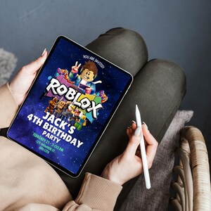 May include: A digital tablet displaying a Roblox-themed birthday party invitation. The invitation features the Roblox logo, a cartoon character, and text that reads "Jack's 4th Birthday Party". The tablet is held by a person, with a stylus in hand.