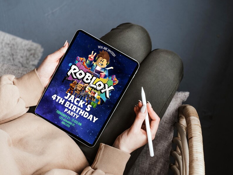 May include: A digital tablet displaying a Roblox-themed birthday party invitation. The invitation features the Roblox logo, a cartoon character, and text that reads "Jack's 4th Birthday Party". The tablet is held by a person, with a stylus in hand.